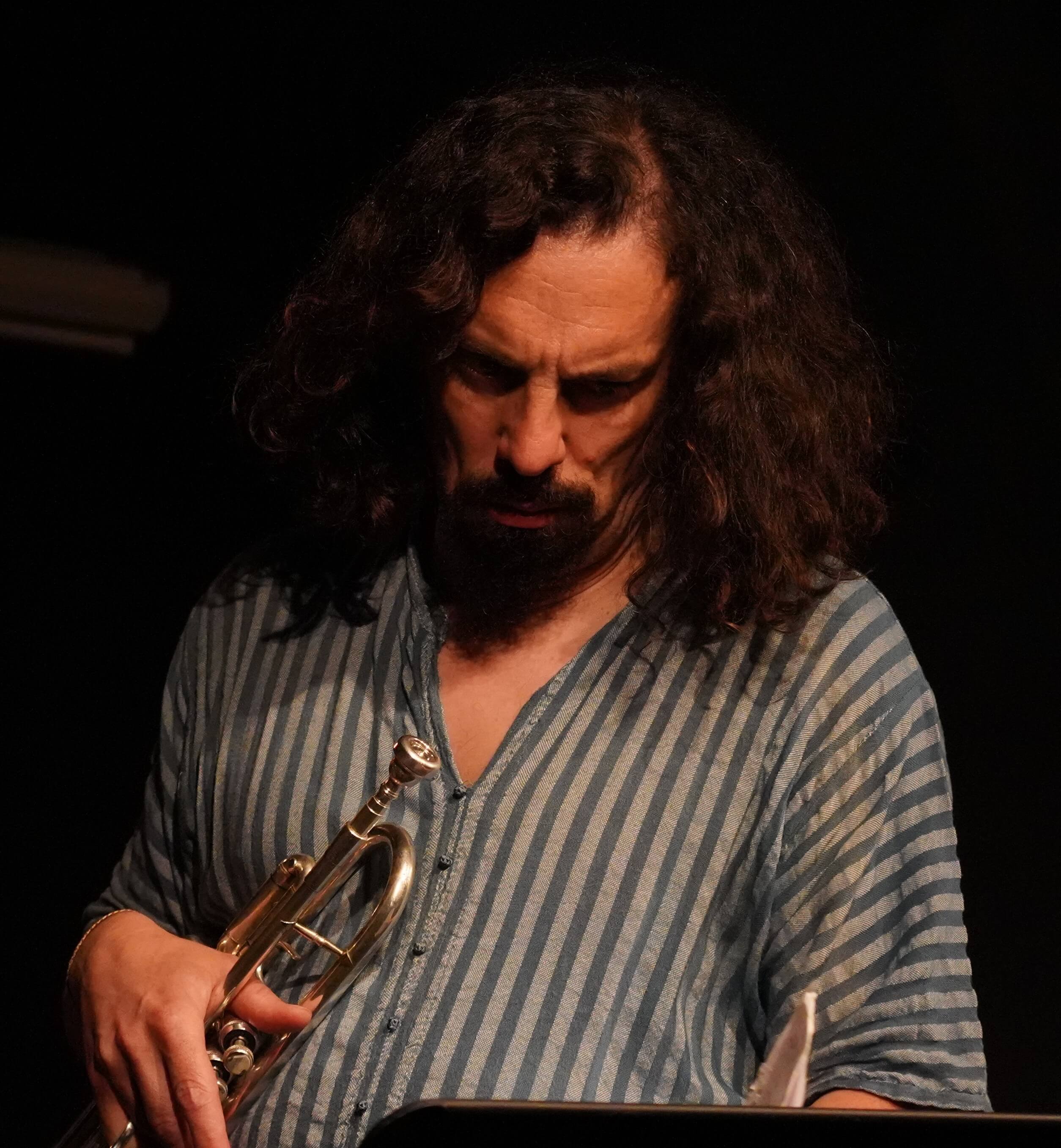 Trompeter hält eine silberne Trompete im Bühnenlicht vor dunklem Hintergrund.