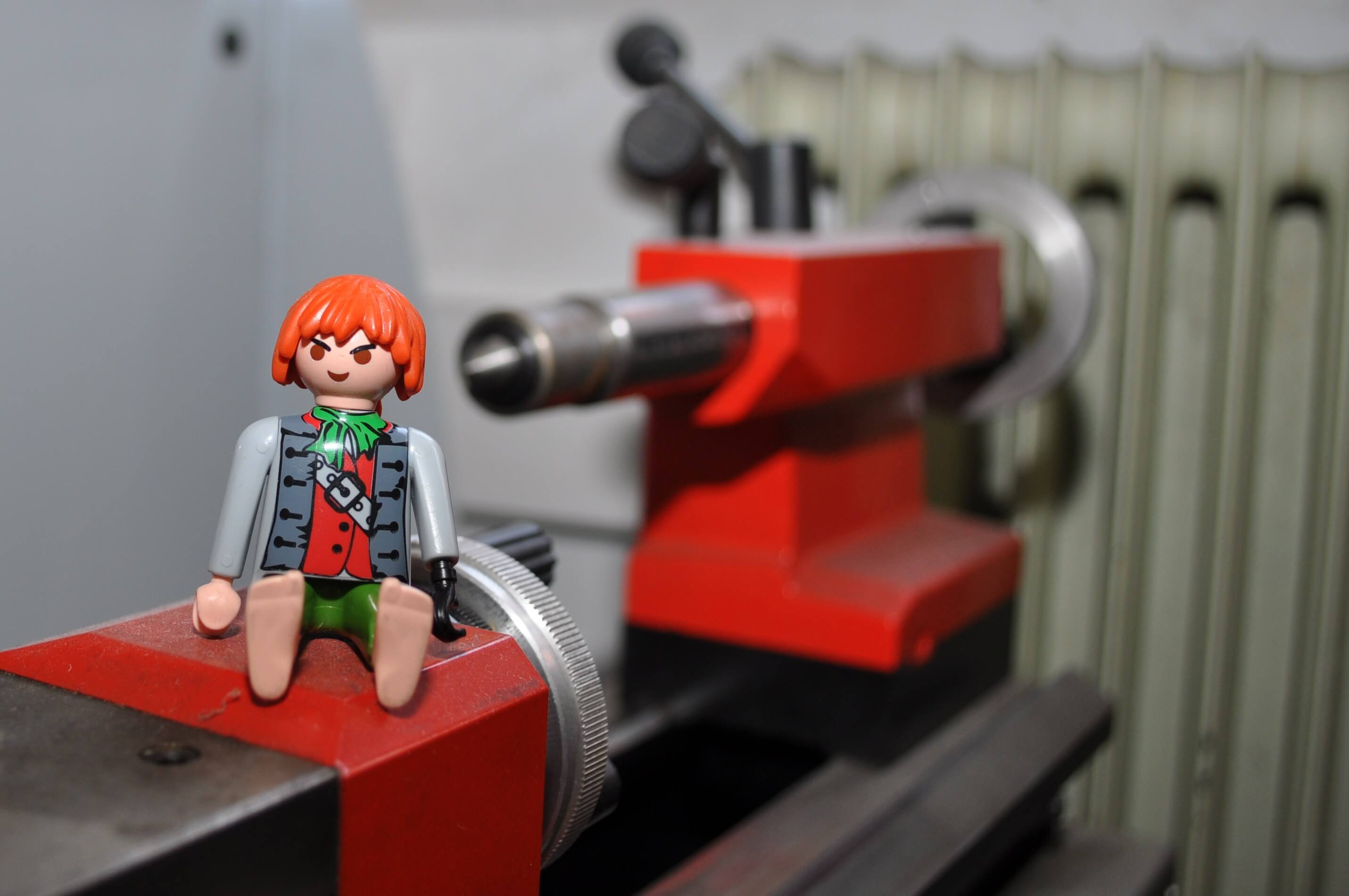 Playmobil-Piratenfigur sitzt auf einer roten Metall-Drehmaschine in einer Werkstatt.